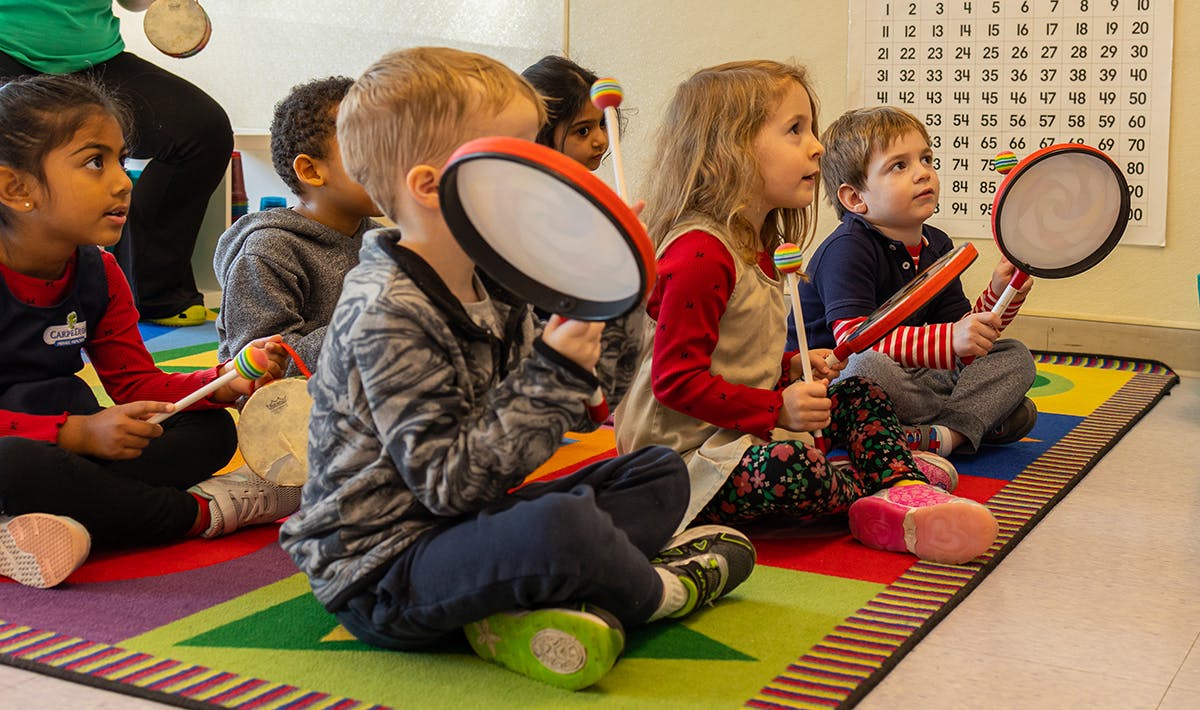 Children sitting on a rug playing with tambourines