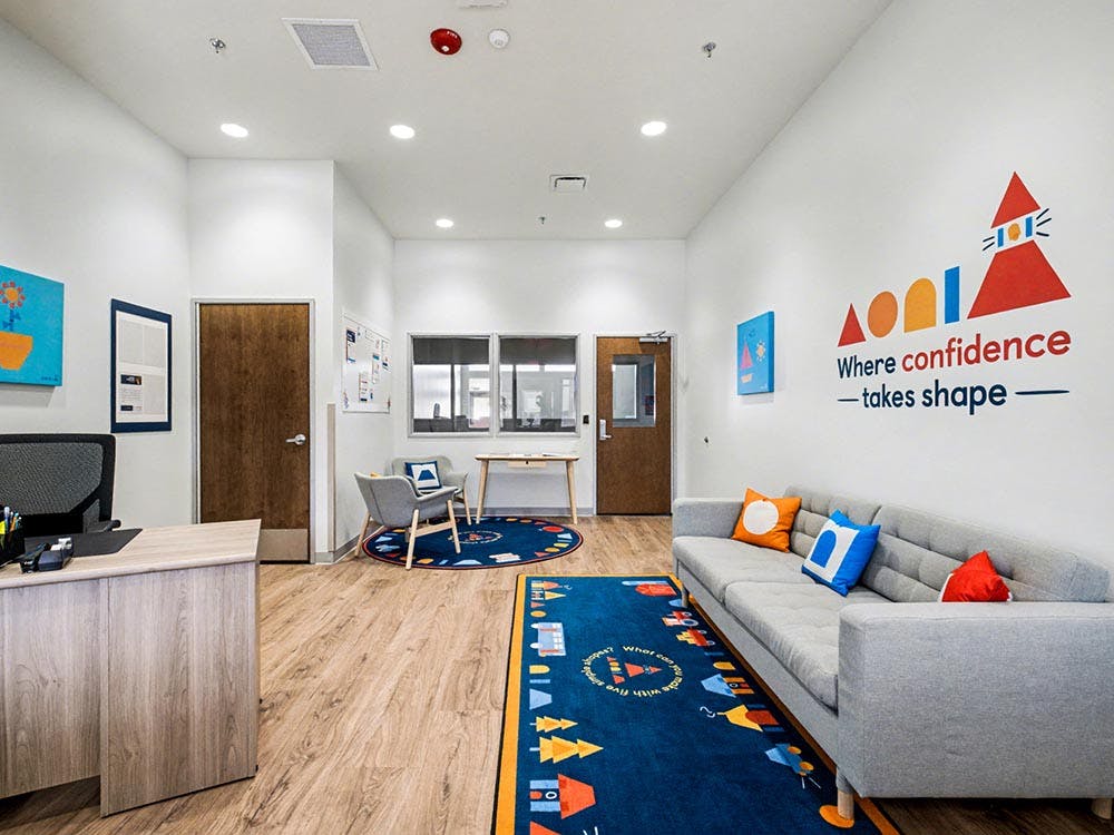 Lobby with a gray sofa, colorful rugs, and a wall decal with text