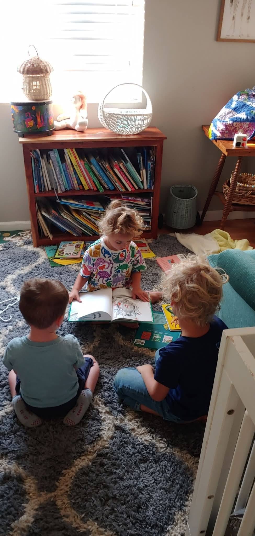Three children sitting on a rug reading a book together