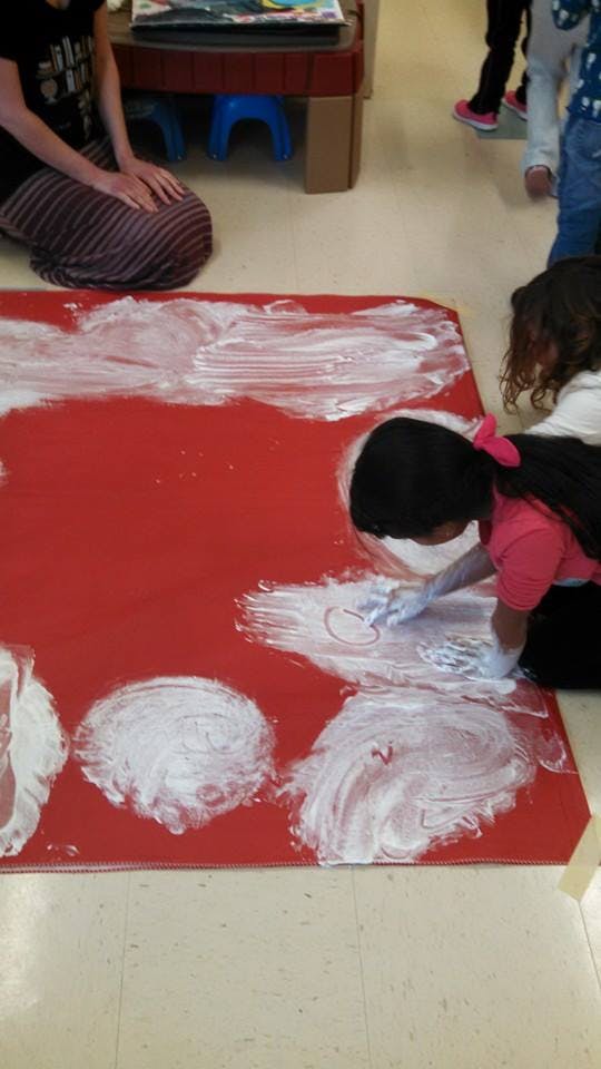 Child finger painting white paint on a red mat