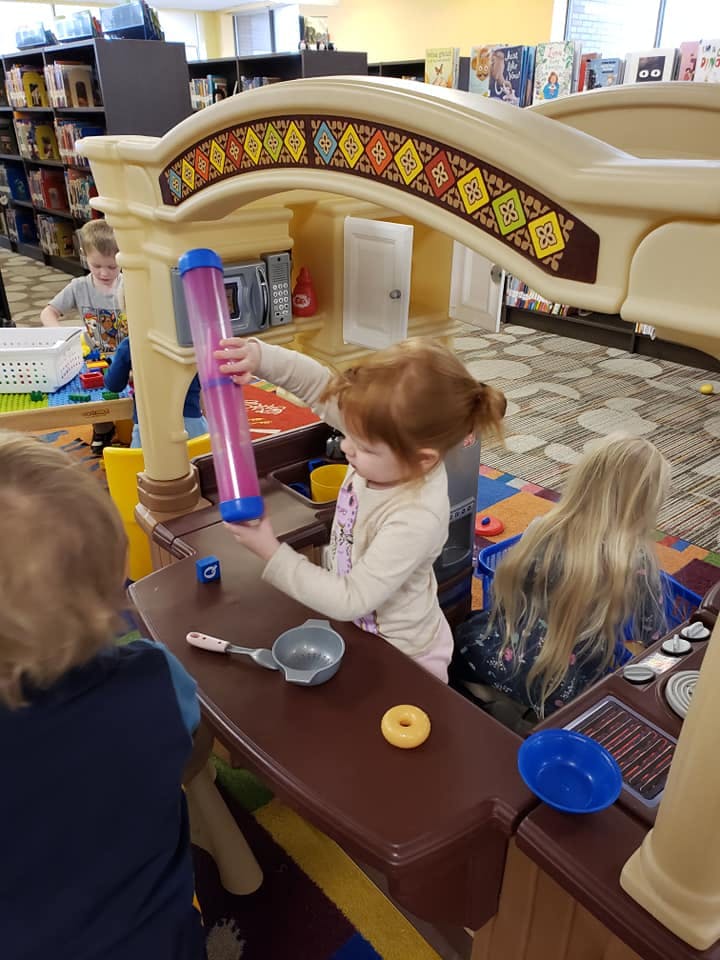 Child playing with a toy kitchen set, holding a pink and blue toy