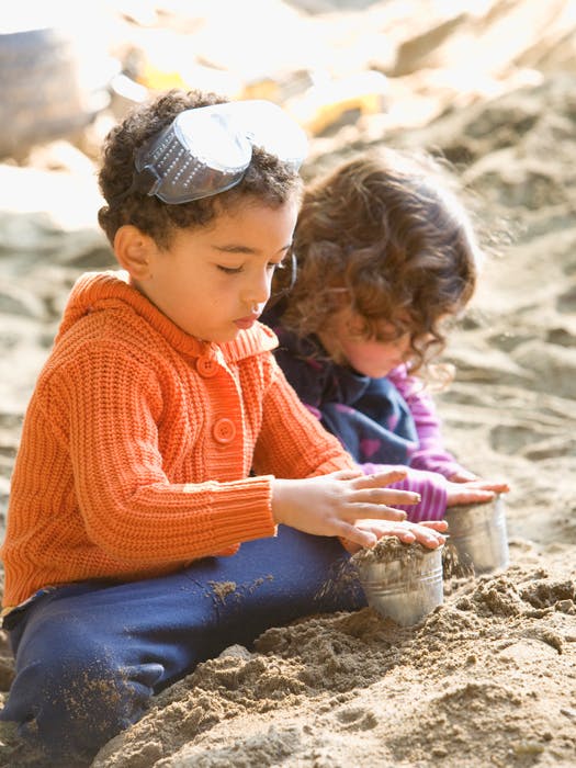 Two children playing in sand with small metal containers