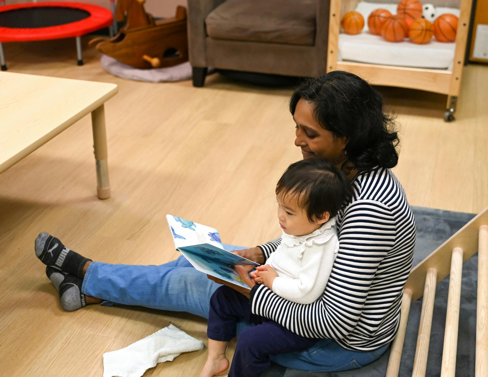 Person sitting on floor holding a child and reading a book