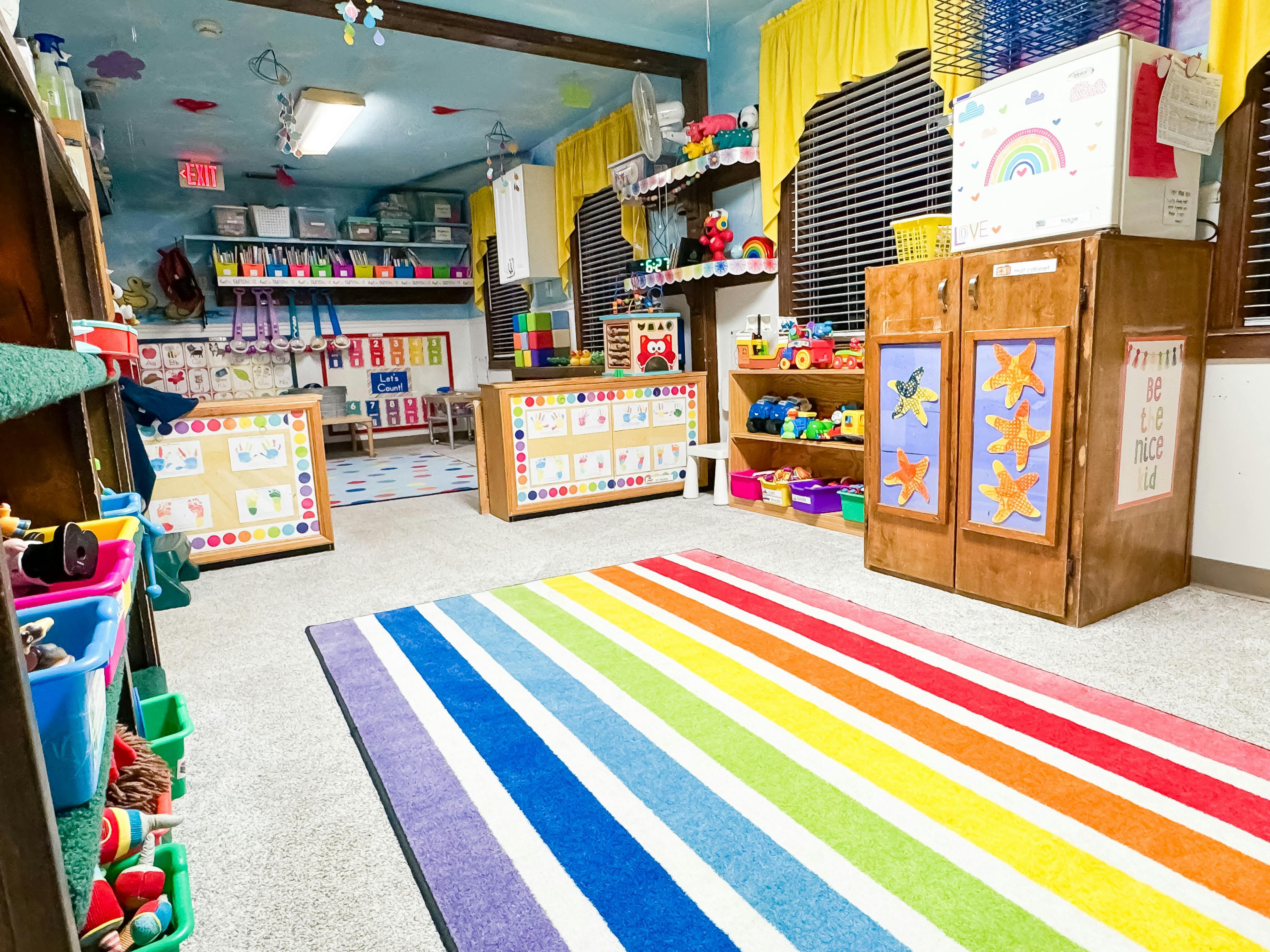 Classroom interior with a rainbow rug, toys, and educational wall displays