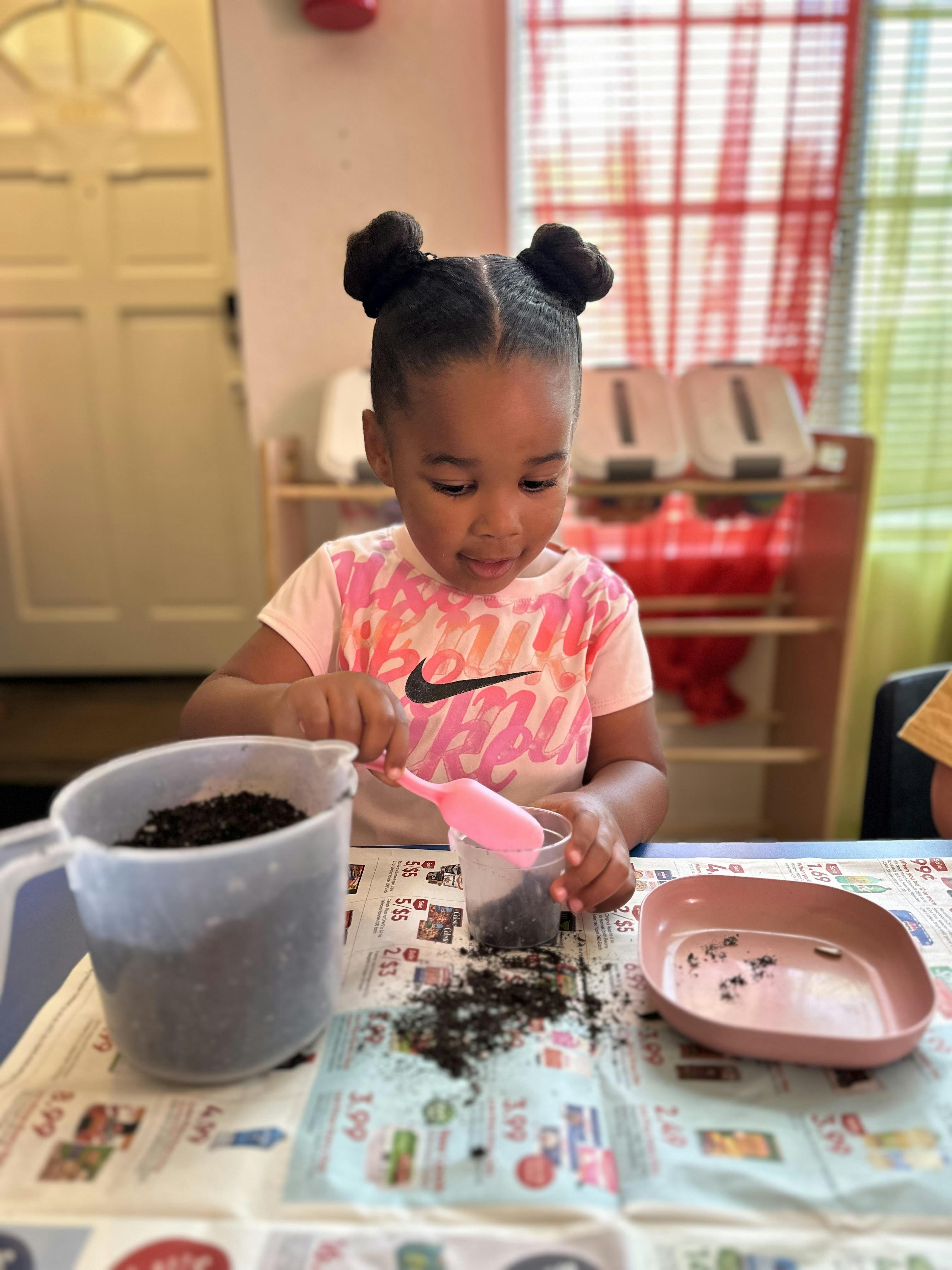 Child scooping soil from a large container into a small cup
