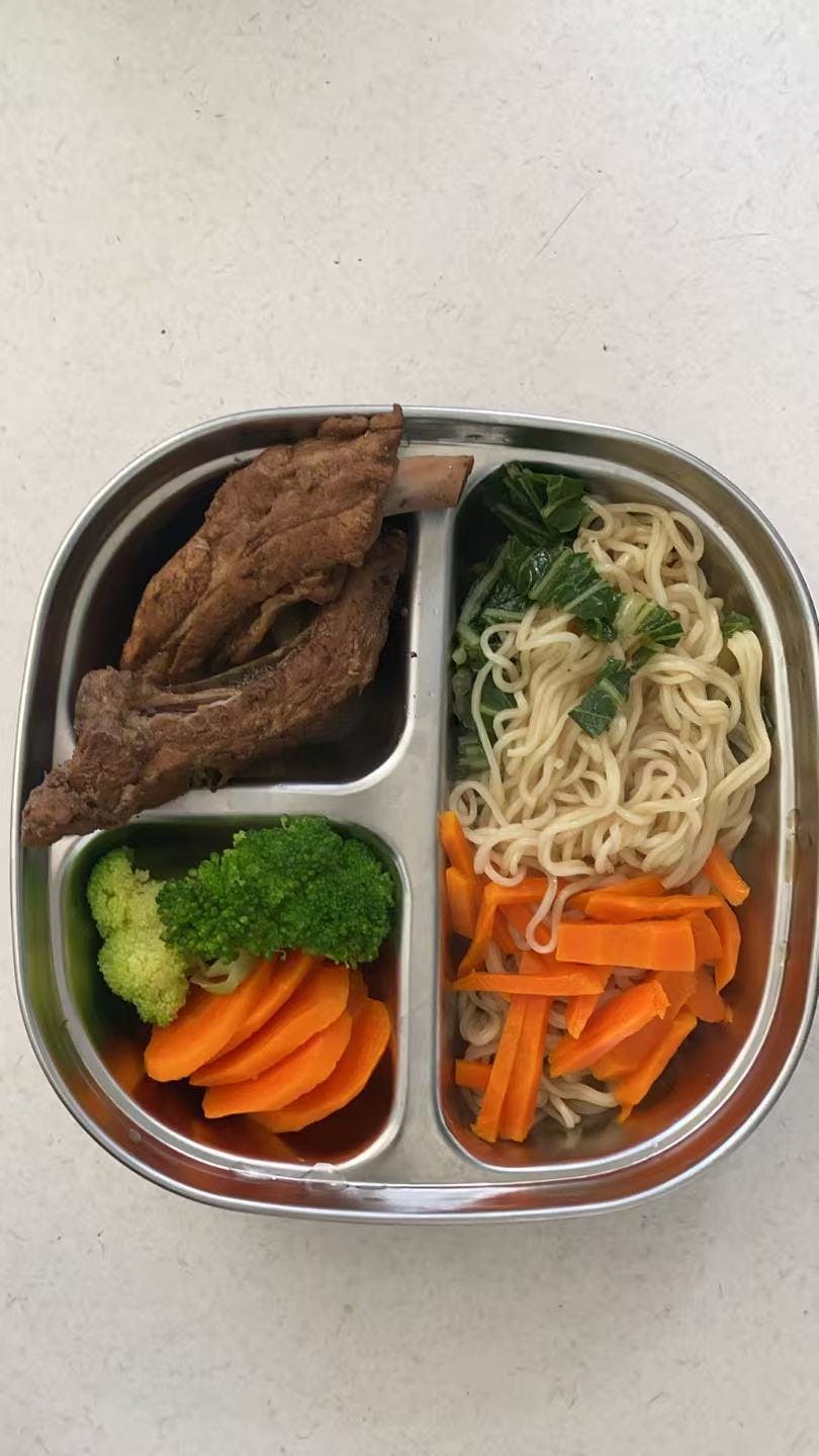 Compartmentalized metal tray with ribs, noodles, broccoli, and sliced carrots
