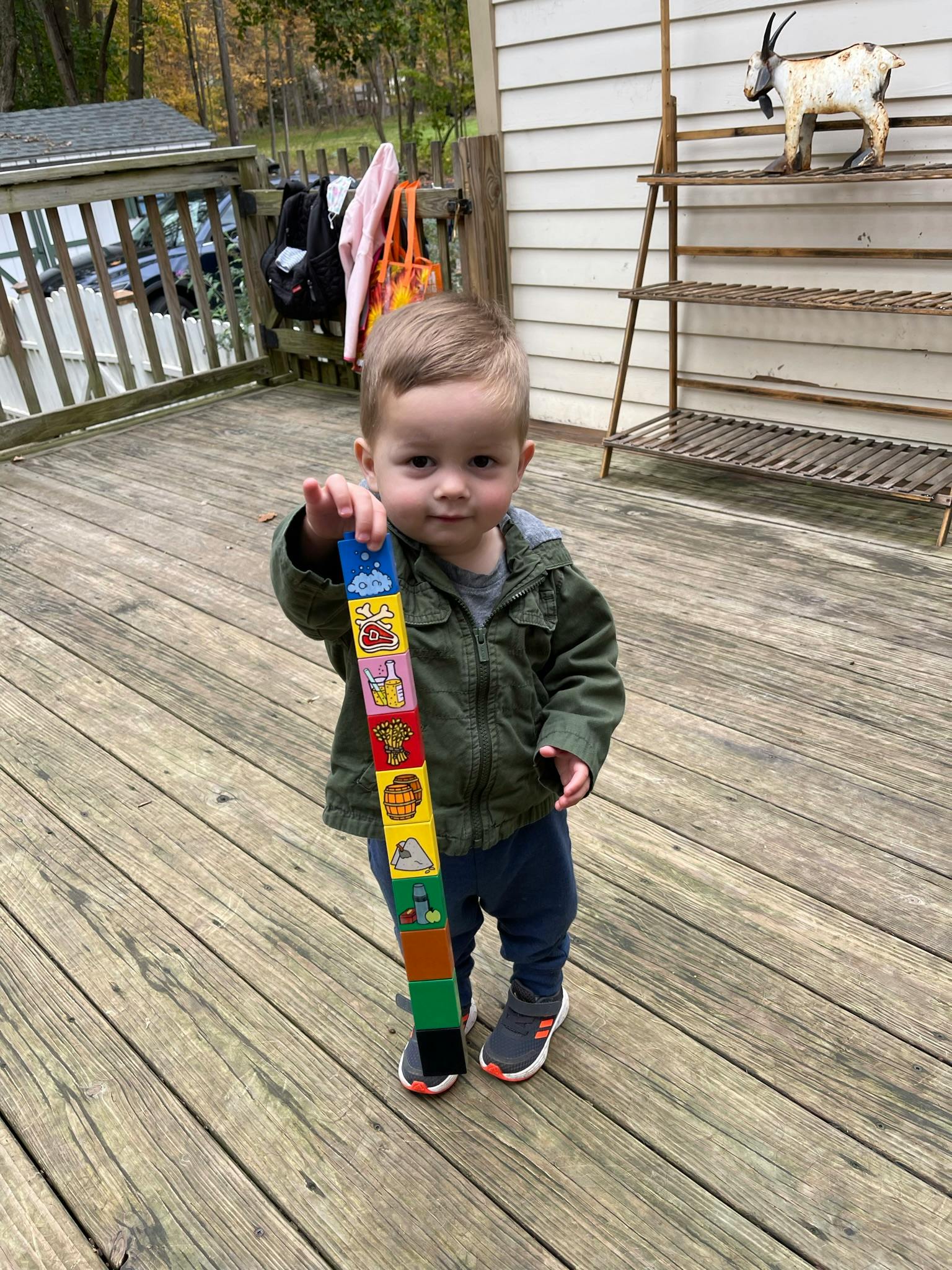 Child holding a stack of colorful blocks on a wooden deck