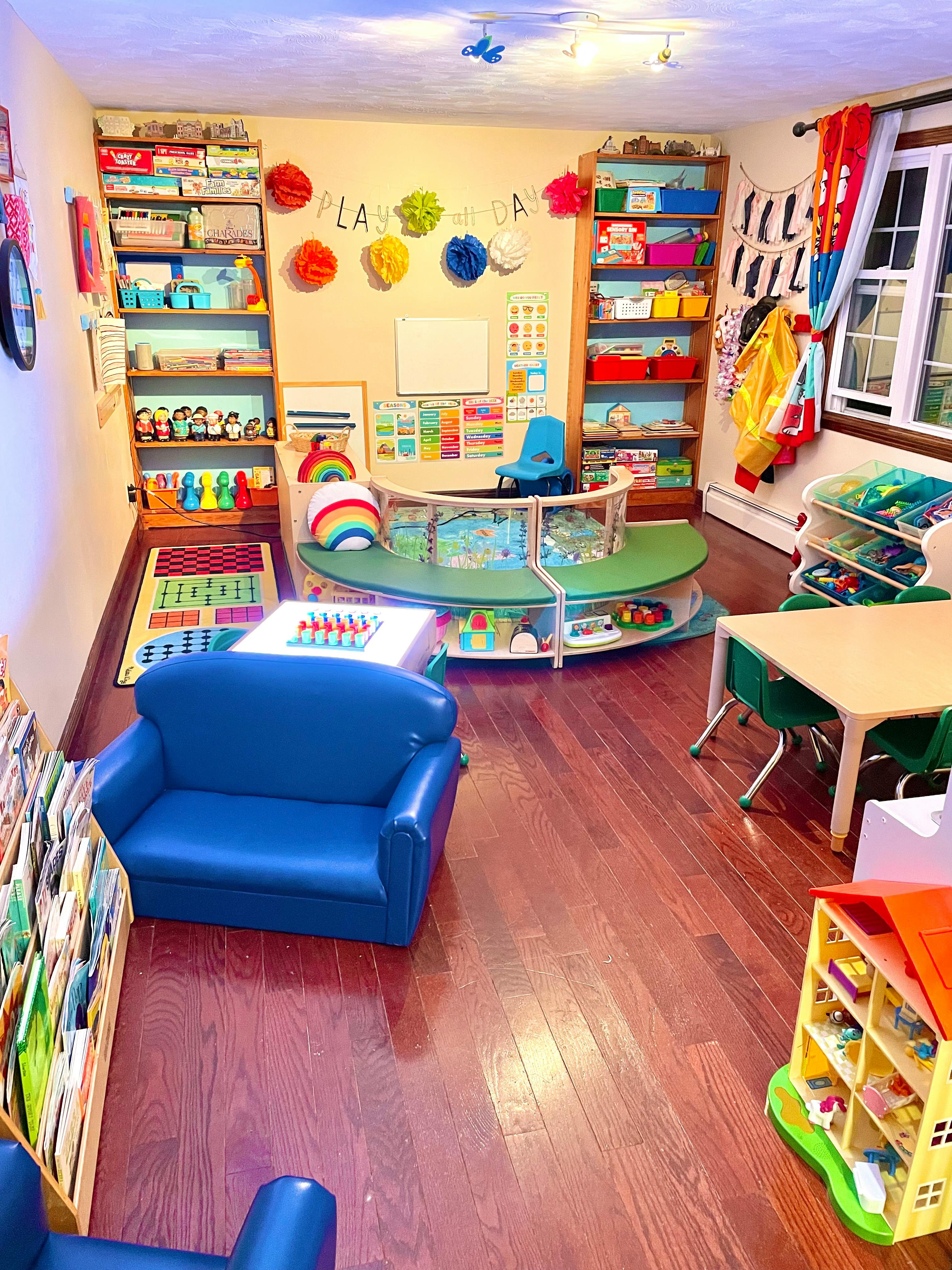 Children's playroom with shelves of toys, small tables, and blue seating