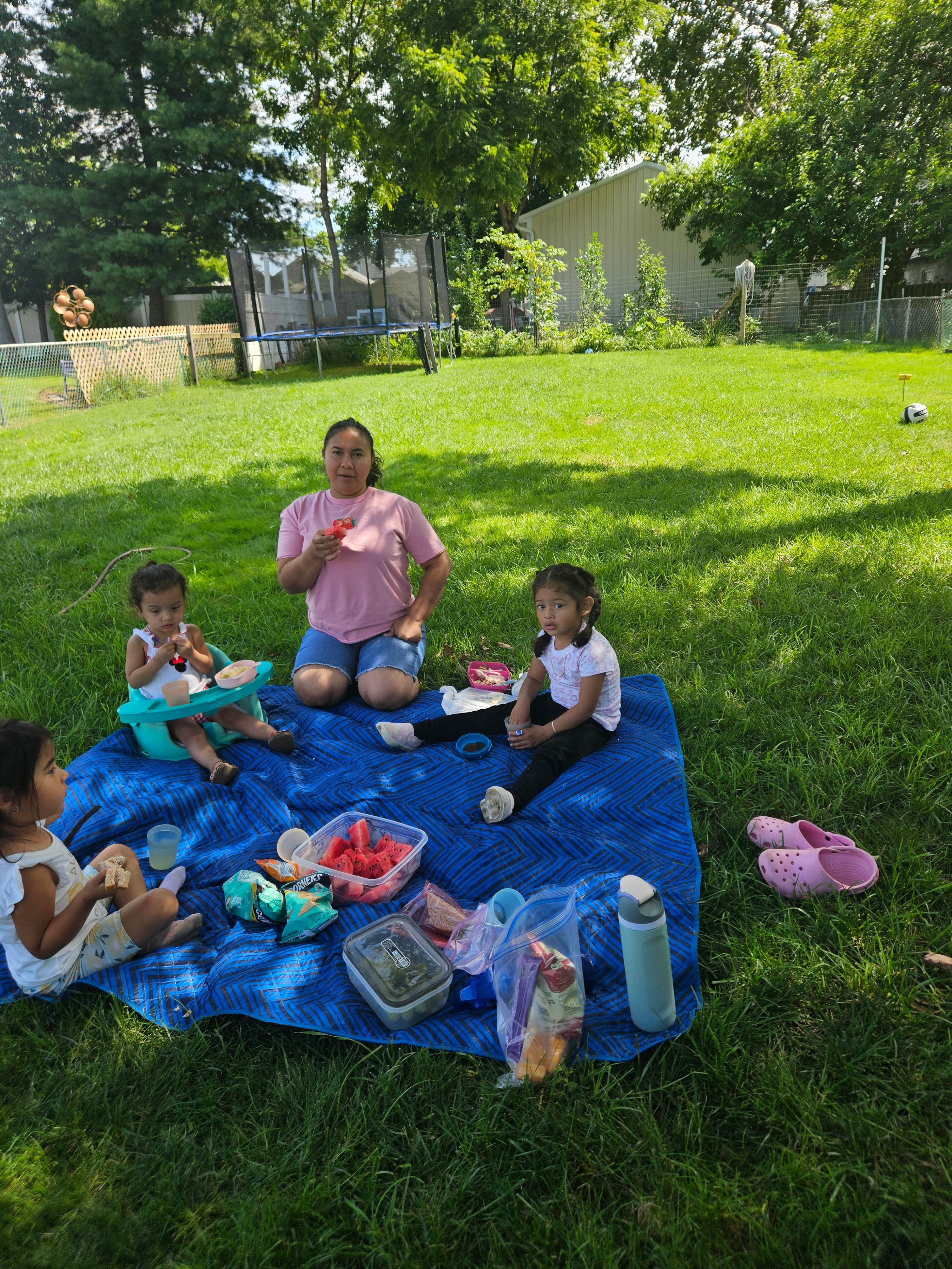 People having a picnic on a blue blanket in a grassy backyard