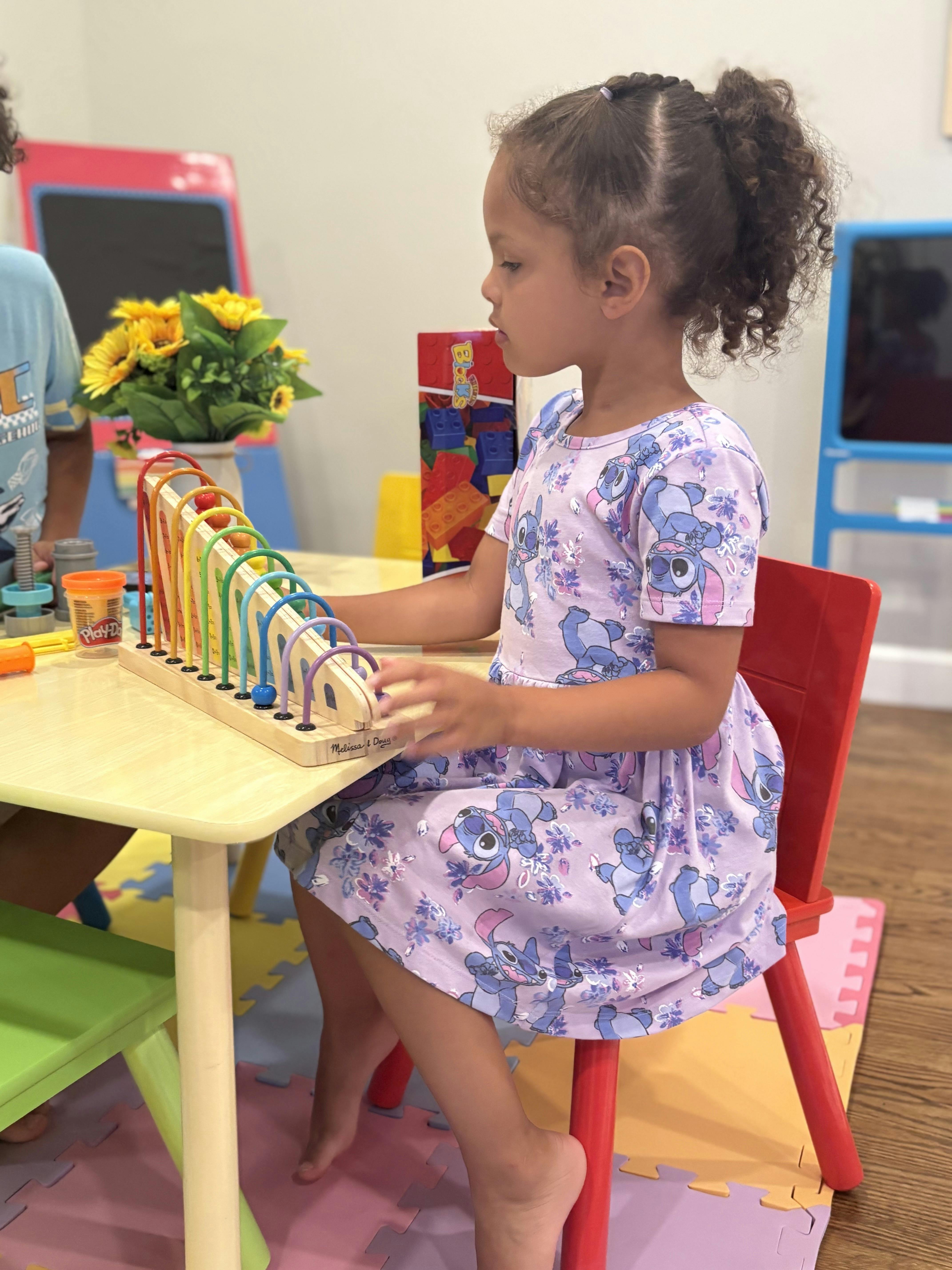 Child sitting at a small table playing with a colorful bead maze toy