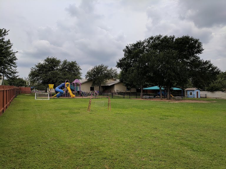 Playground with slides and swings next to a building and large trees