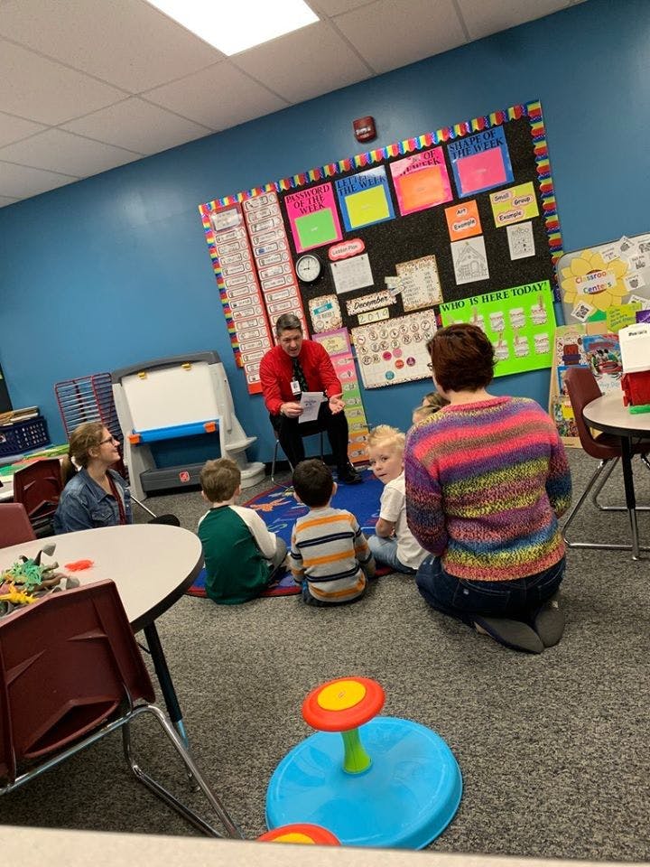 Adult reading to children and another adult sitting on the floor in a classroom
