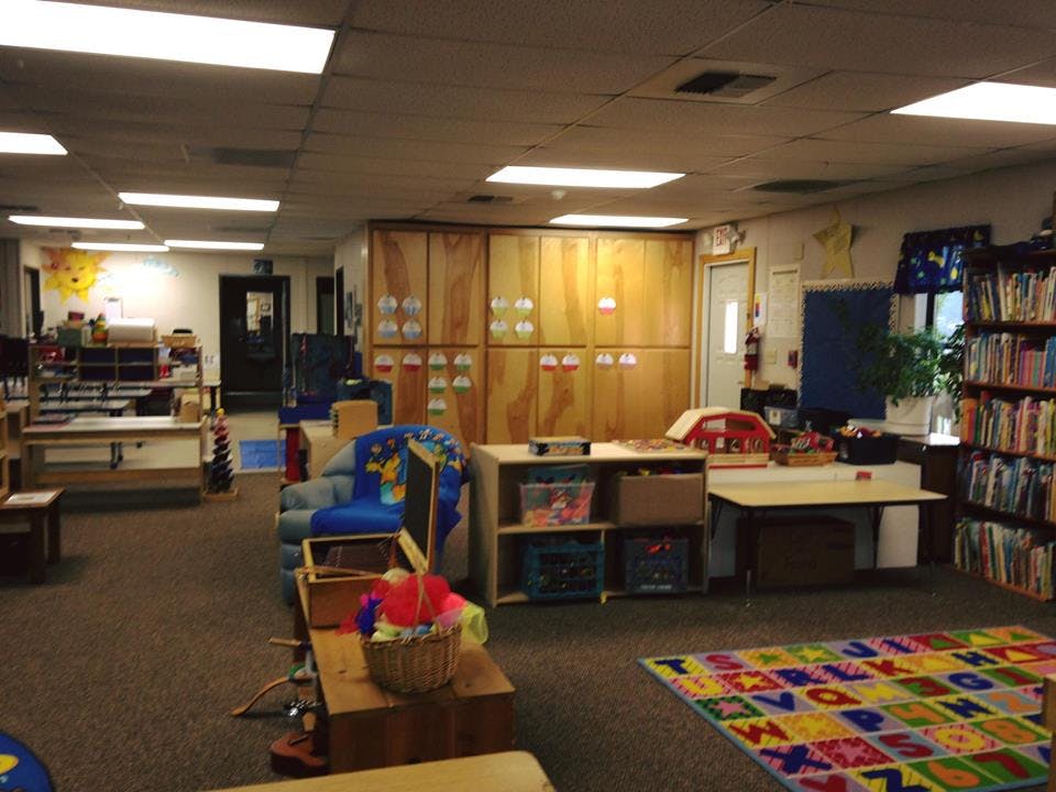 A classroom with a colorful alphabet rug, bookshelves, and wooden cabinets