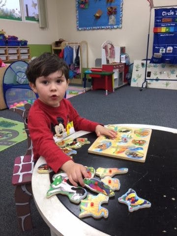 Child playing with a puzzle at a table in a classroom