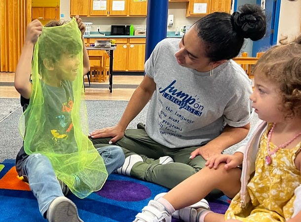 Adult and two children sitting on a rug, one child holding up a sheer green fabric