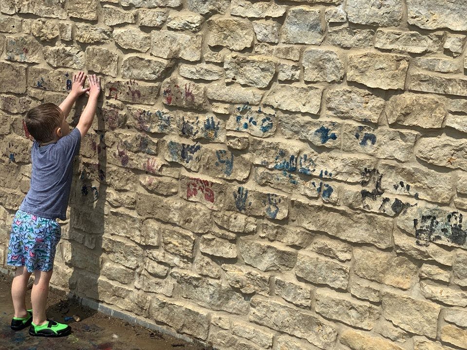 Child reaching up to a stone wall with handprints