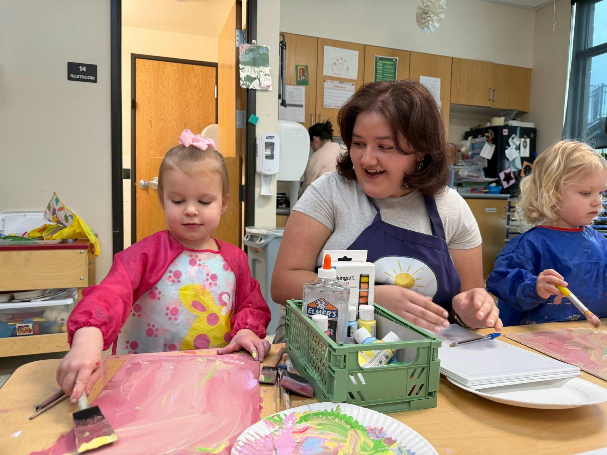 Adult and two children painting at a table in a classroom