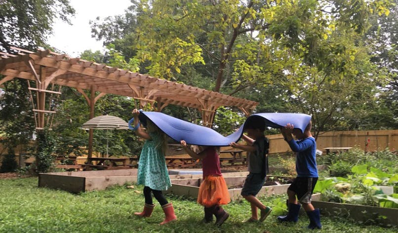Four children holding a blue tarp over their heads outdoors