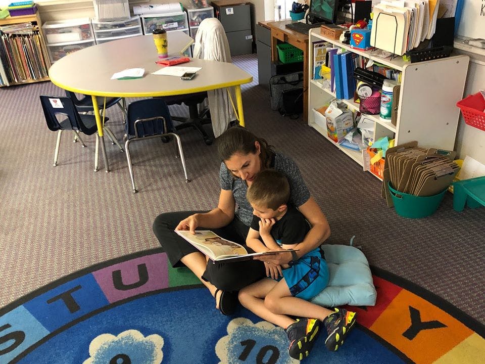 Adult and child sitting on floor reading a book in a classroom