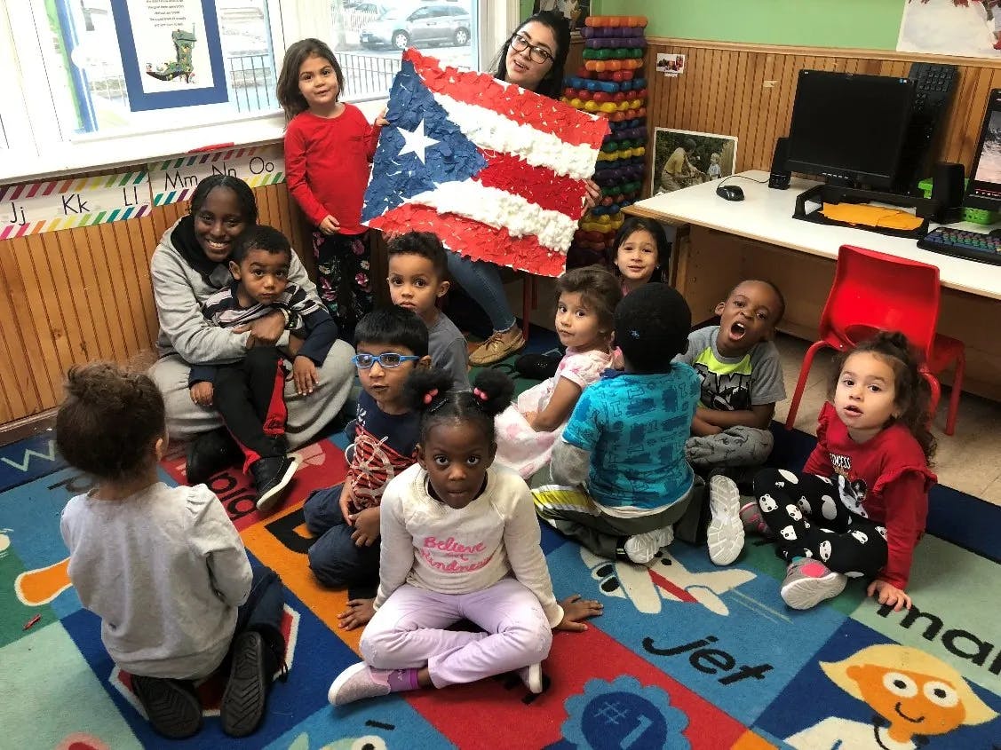 Adults and children sitting on a rug, one adult holding a Puerto Rican flag