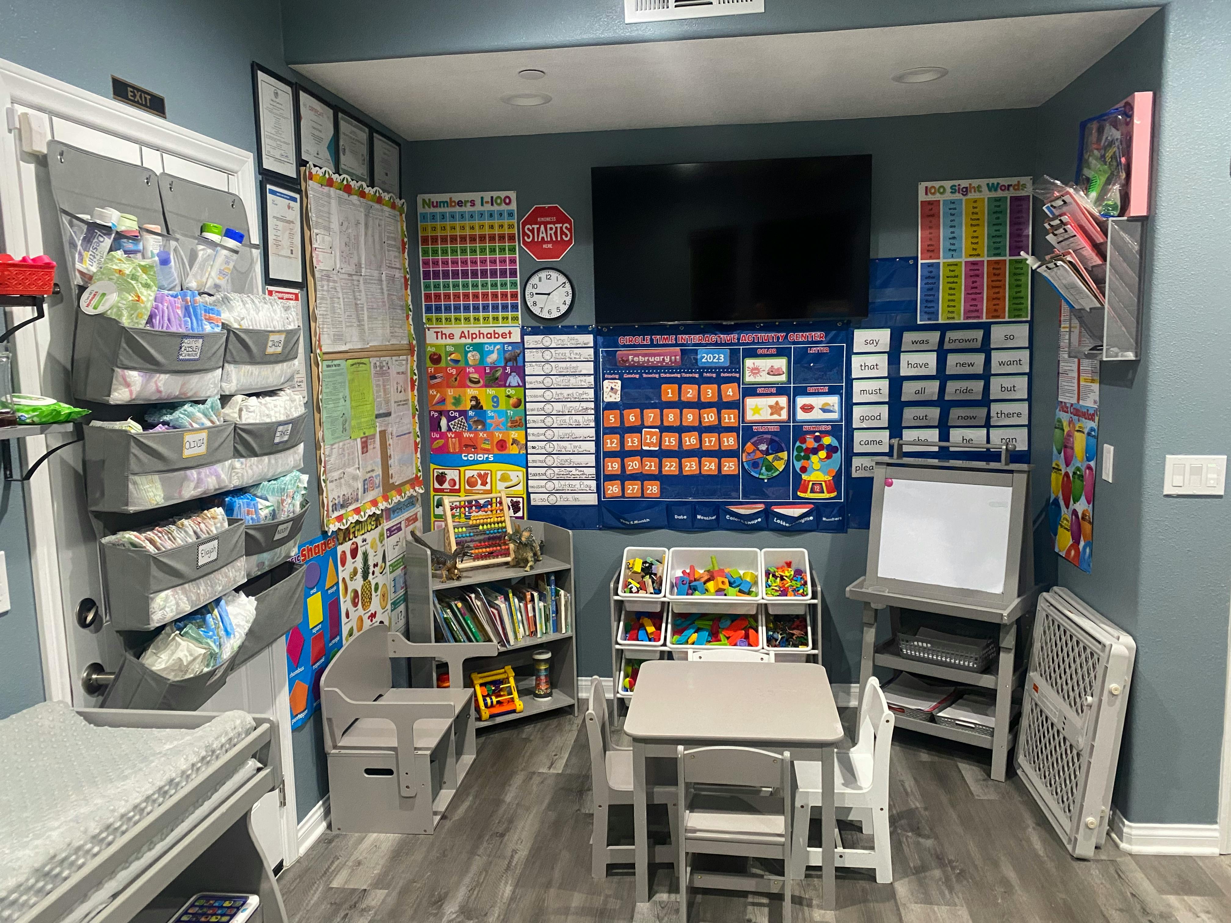 A classroom with a small table and chairs, shelves with books and toys, and educational posters