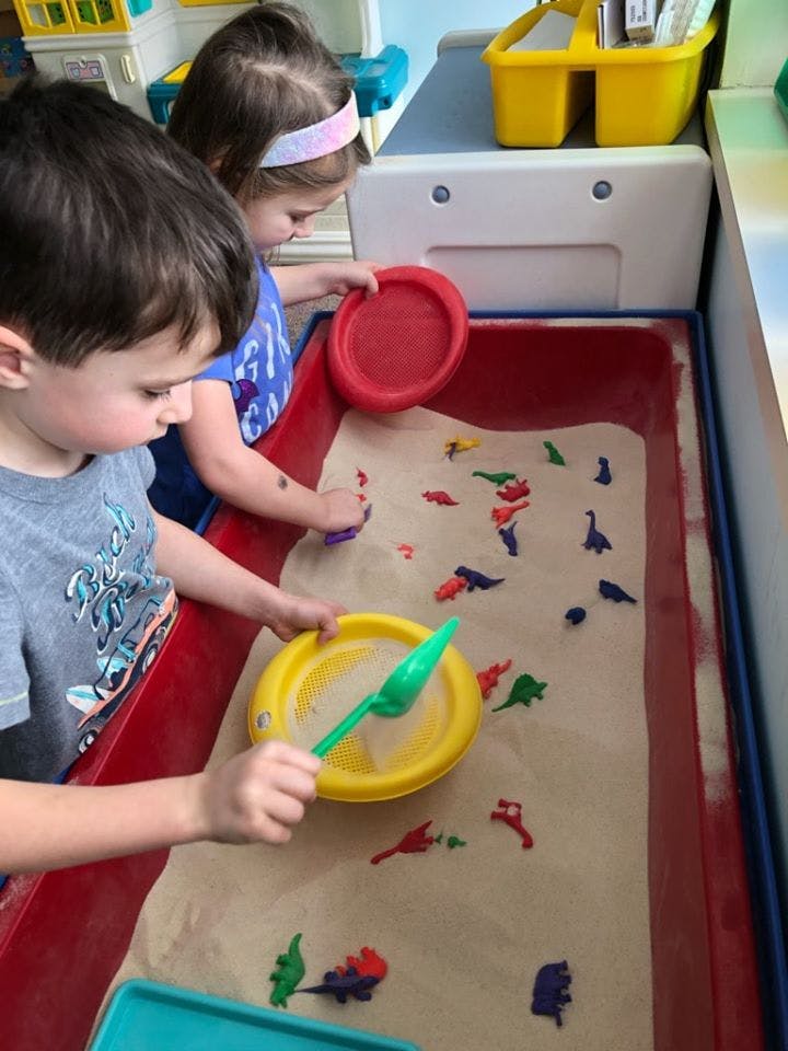 Two children playing with sand and small toys in a sand table