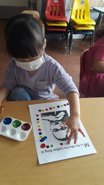 Child in a mask painting a picture of Martin Luther King Jr.