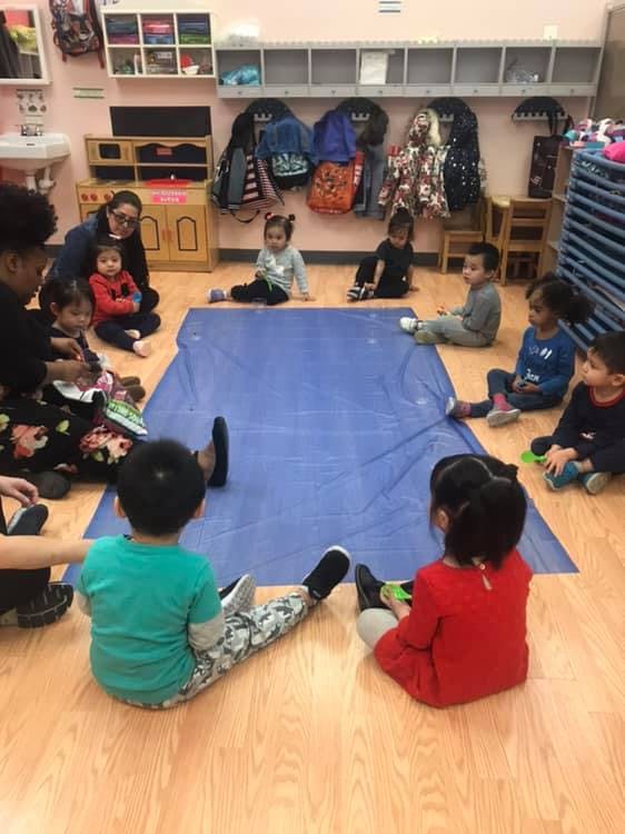 Adults and children sitting on the floor around a blue mat in a classroom