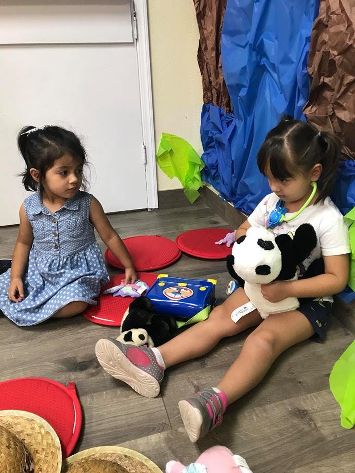 Two children playing on the floor, one holding a stuffed panda