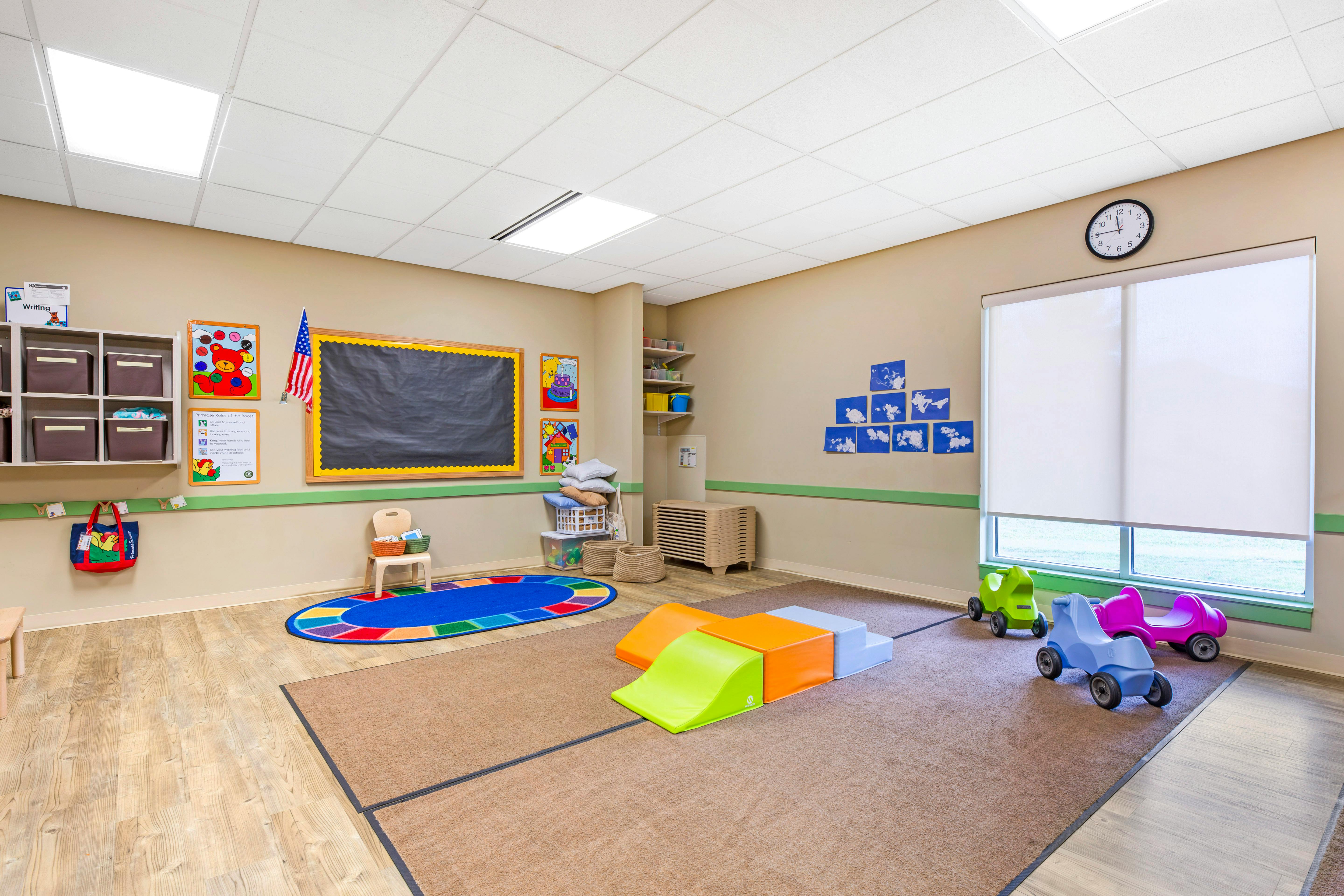 Classroom with a chalkboard, colorful rug, climbing blocks, and ride-on toys