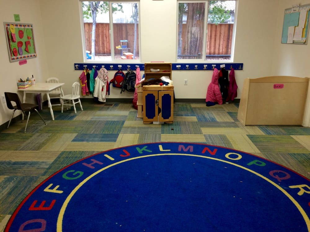 Classroom with an alphabet rug, small table and chairs, and coat hooks