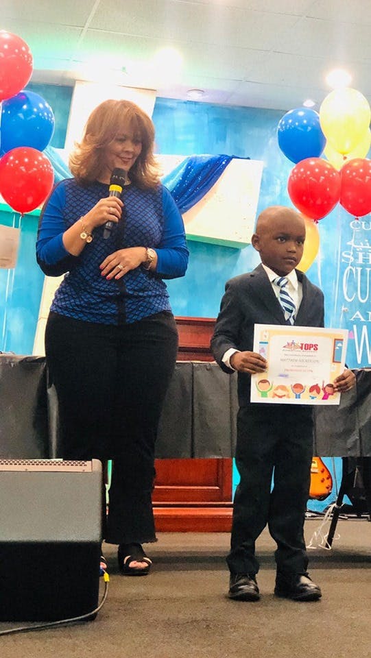Person speaking into a microphone next to a child holding a certificate