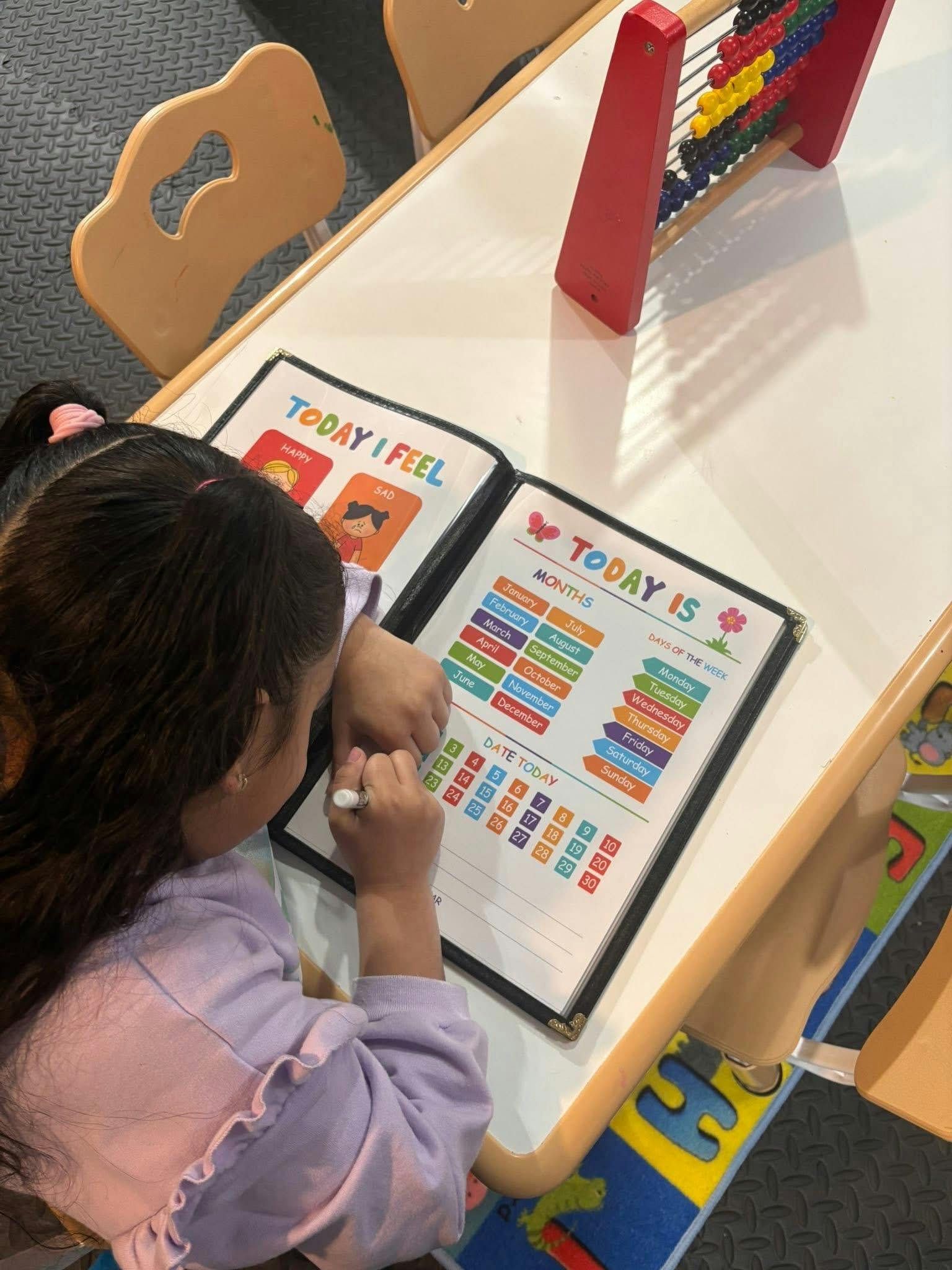 Child writing on a calendar chart at a desk