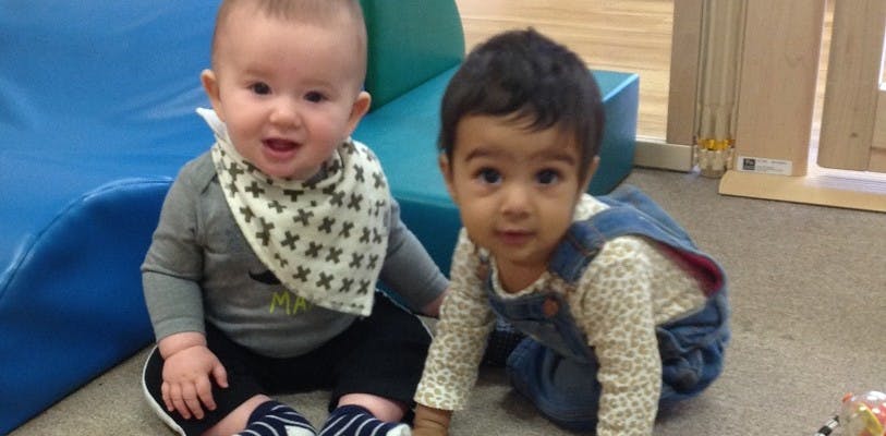 Two children on the floor, one sitting and one crawling