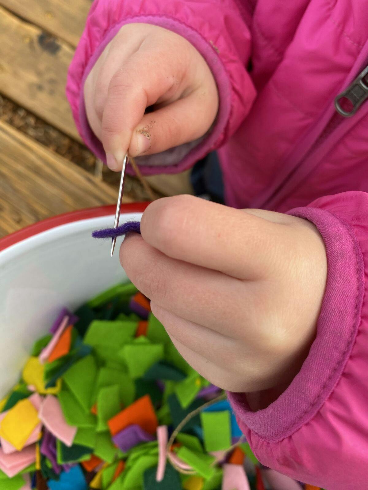 Child's hands threading a needle through a piece of fabric
