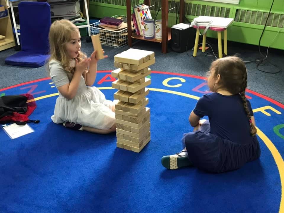 Two children playing with a Jenga tower on a blue rug