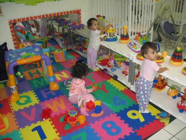 Three children playing with toys in a room with an alphabet mat