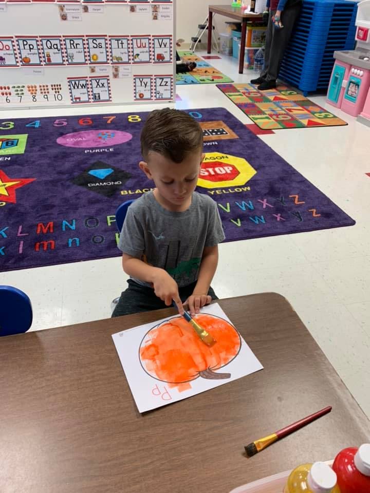 Child painting a pumpkin drawing in a classroom