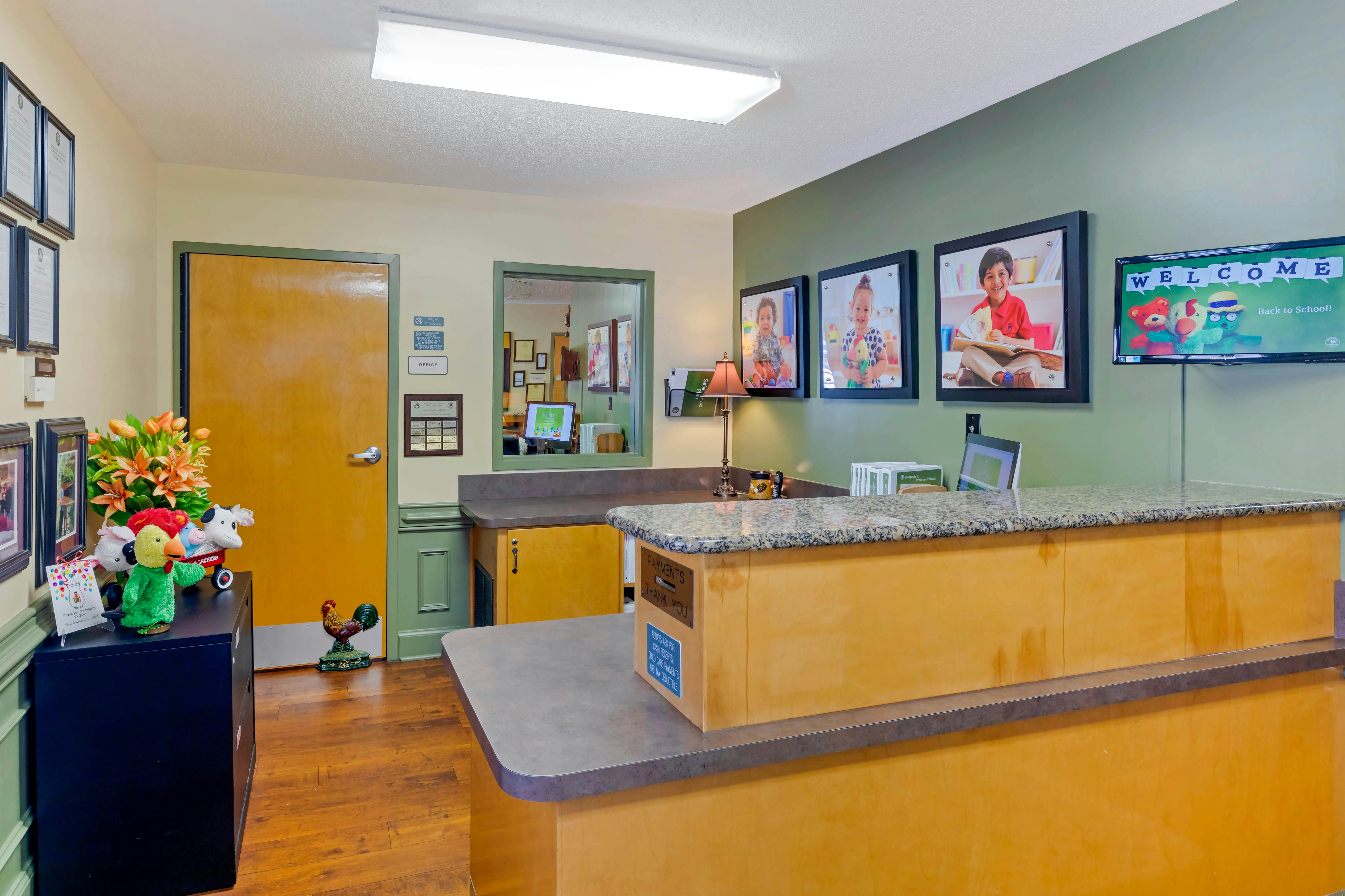 Reception area with a counter, a screen showing "Welcome Back to School!", and child photos