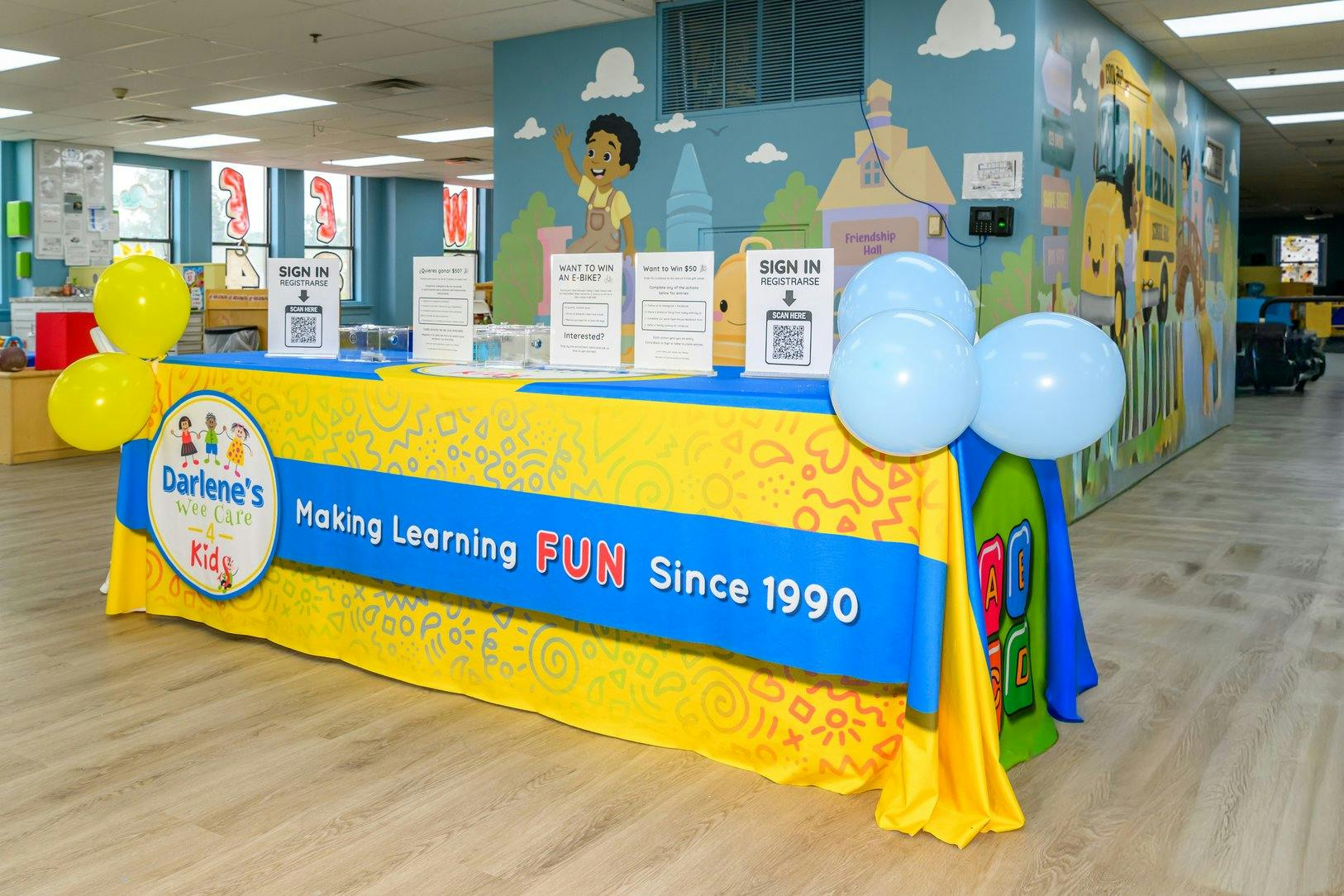 Sign-in table with Darlene's Wee Care 4 Kids banner and balloons