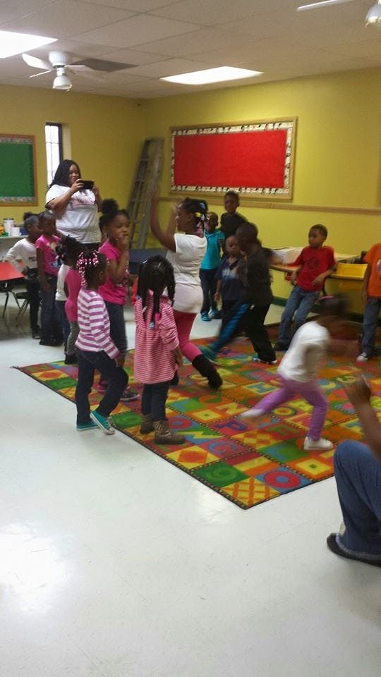 Adult filming children dancing on a colorful mat in a classroom