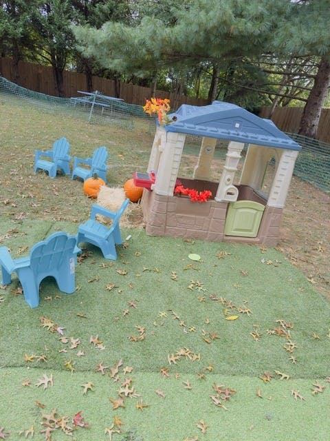 Plastic playhouse with toy chairs and pumpkins in a yard with autumn leaves