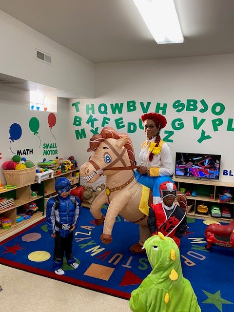 Person in cowgirl costume riding an inflatable horse with children in costumes