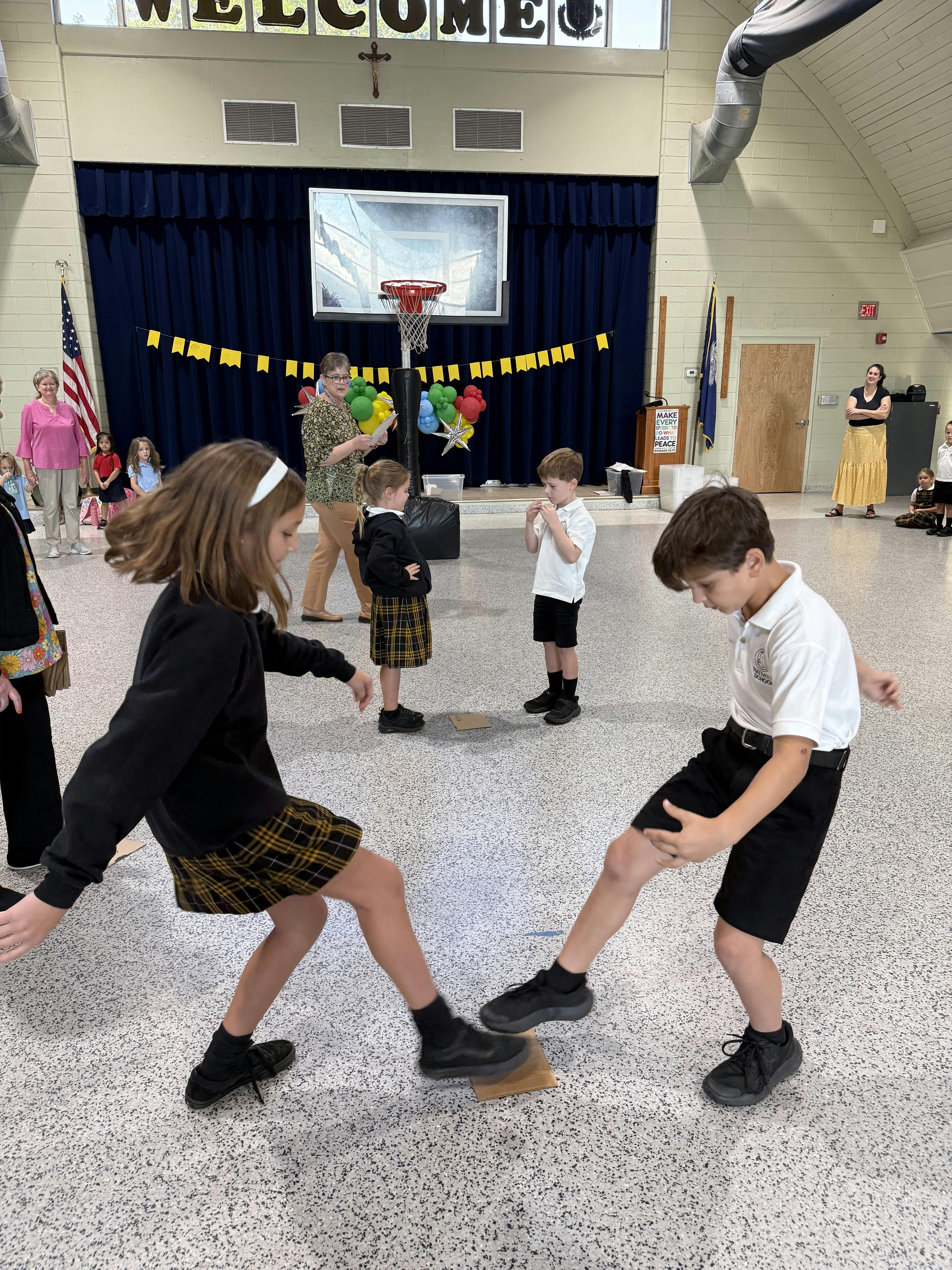 Children in uniforms playing a game with cardboard on a gym floor