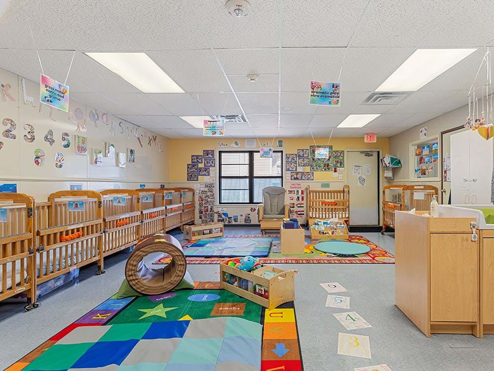 Baby room with multiple cribs, colorful play mats, and learning decorations