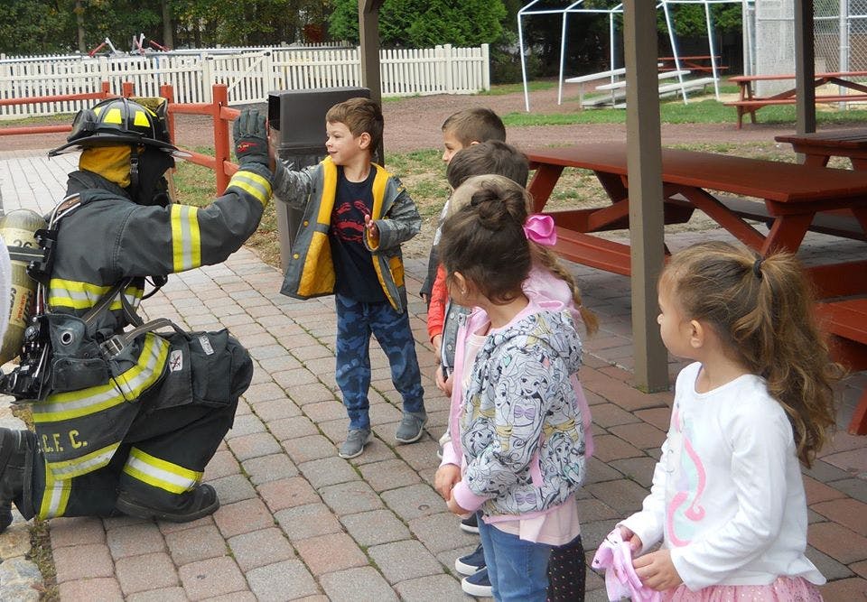 Firefighter kneeling and high-fiving a child, other children watching
