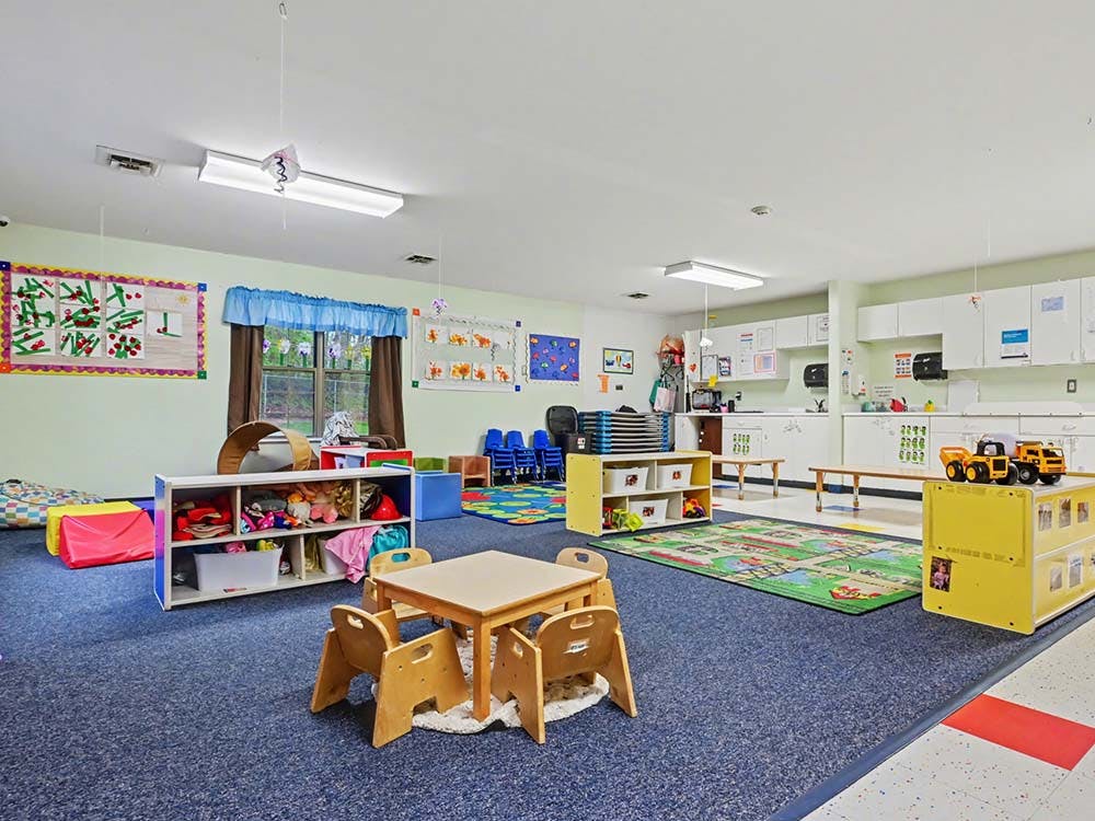 A classroom with small tables, chairs, toy shelves, and play mats