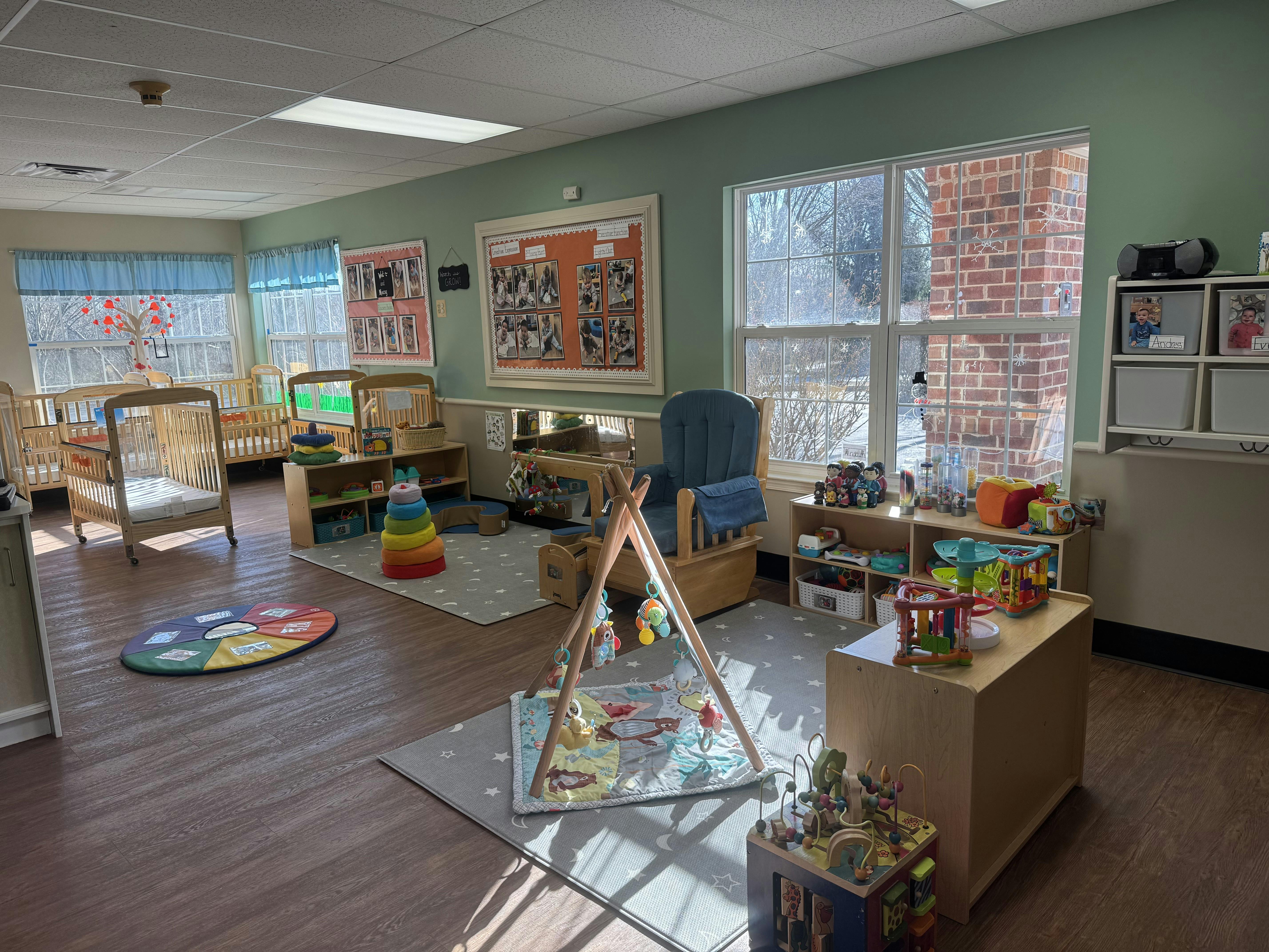 A brightly lit nursery room with multiple cribs, a rocking chair, and toys