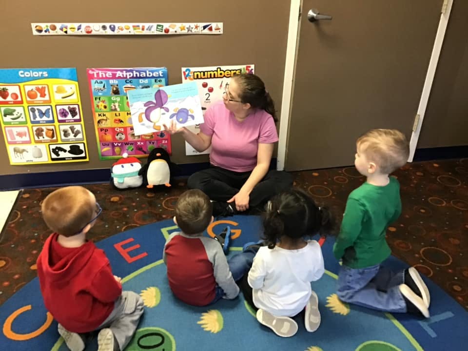 Adult reading a book to four children sitting on a rug