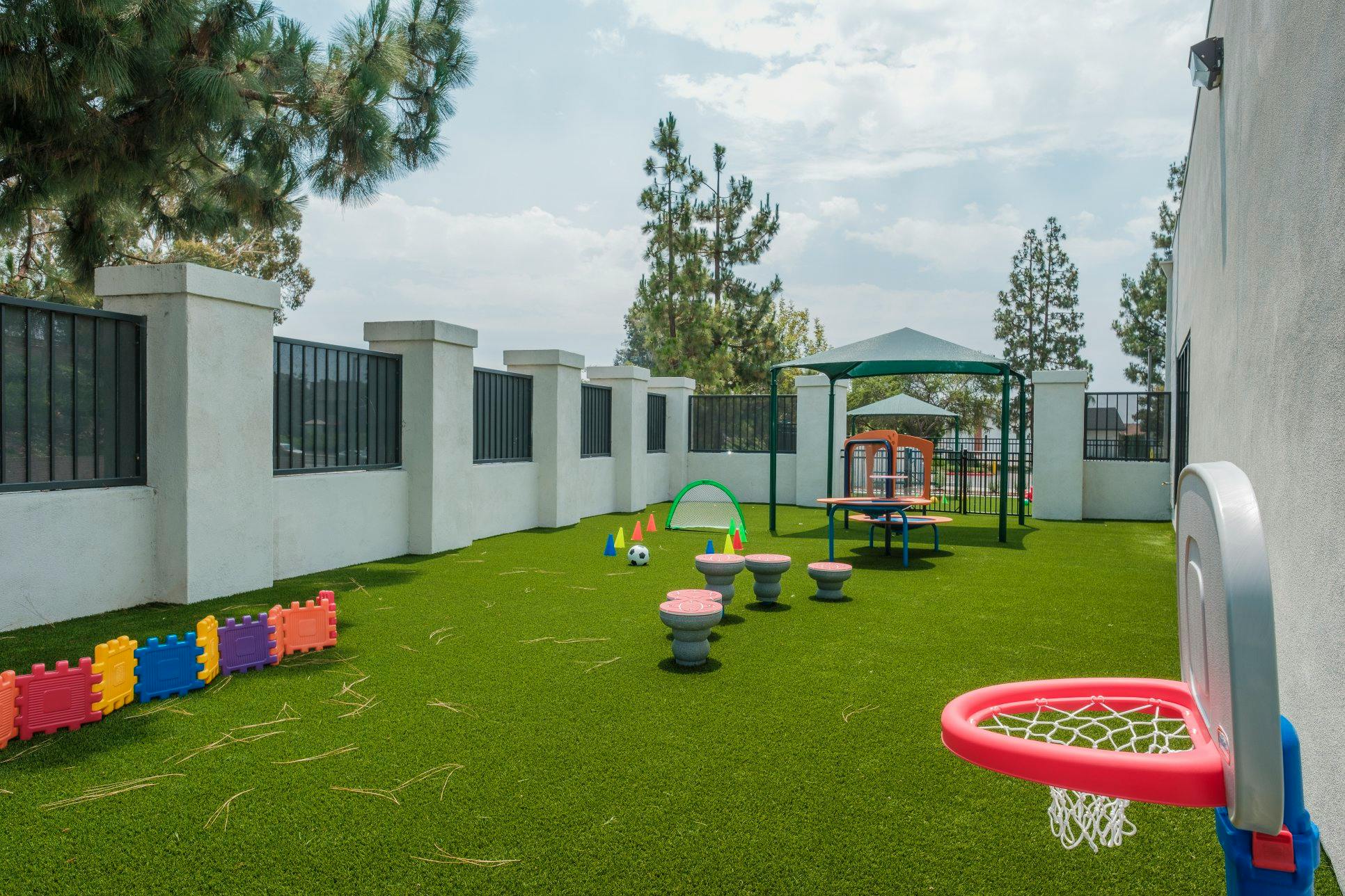 An outdoor play area with artificial turf, a small soccer goal, and a basketball hoop